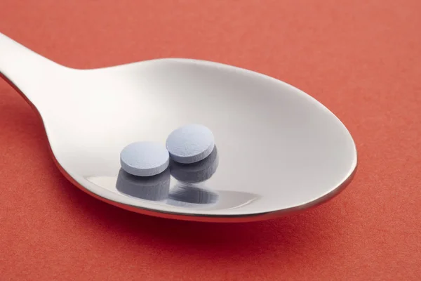 Píldoras y cuchara detalle. Fondo rojo. Tratamiento de medicamentos. Él... — Foto de Stock