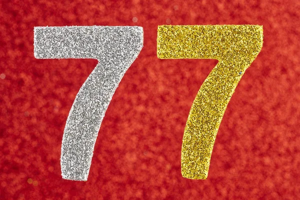 Number seventy-seven yellow silver color over a red background. — Stock Photo, Image