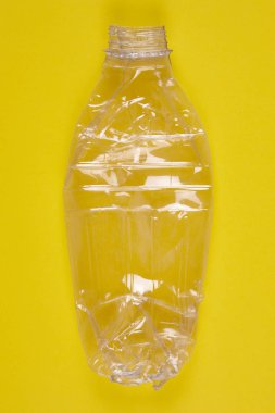 Sarı arka plana sahip ezilmiş plastik şişe. Geri dönüşümlü çöp.