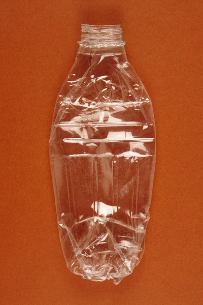 Geplette plastic fles met bruine achtergrond. Gerecycled afval. — Stockfoto