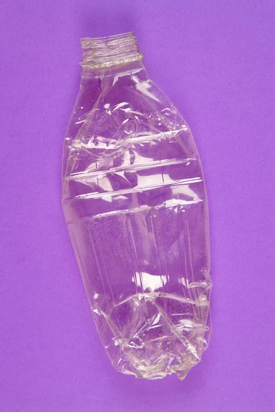 Bottiglia di plastica schiacciata con sfondo viola. Spazzatura riciclata . — Foto Stock