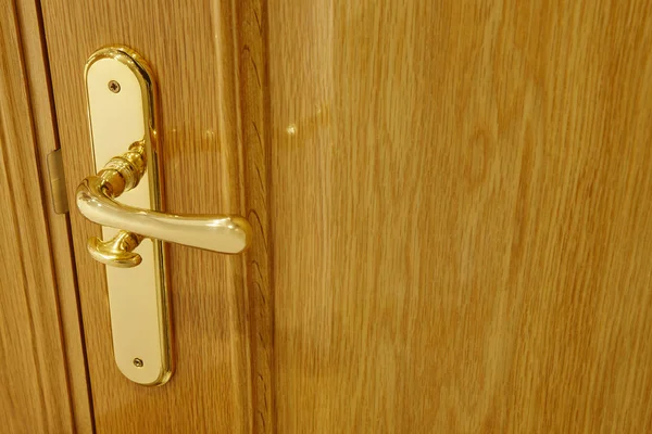 Golden door knob detail on an oak wooden door