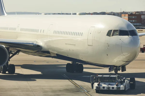 Låg lastbil bogserar ett flygplan på flygplatsens landningsbana. Transportindustri — Stockfoto