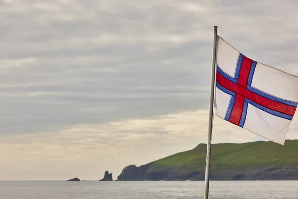 Faerské ostrovy, vlajka vlnící se na západě slunce. Faerská zelená krajina — Stock fotografie