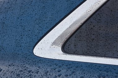 Metalik bir arabanın camına yağmur damlaları düşer. Otomobil ayrıntıları