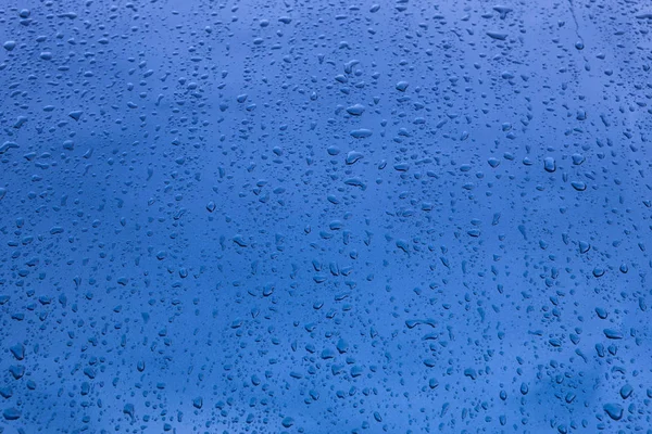 Cadute di pioggia sulla carrozzeria di un veicolo blu. Sfondo bagnato — Foto Stock
