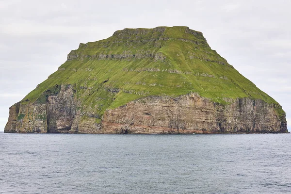 Rotsachtige eiland met groene hellingen in de Faeröer archipel en oceaan — Stockfoto