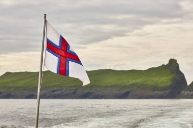 Faroe Adaları bayrağı gün batımında gökyüzünde dalgalanıyor. Faroe yeşil adaları manzarası