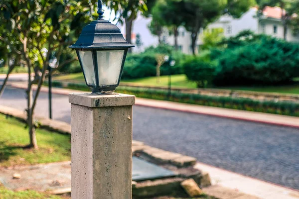 Eine Straßenlaterne auf einer grünen Rasenfläche in einem Park in der Nähe eines Steinweges für Spaziergänge in einem Sommergarten. — Stockfoto