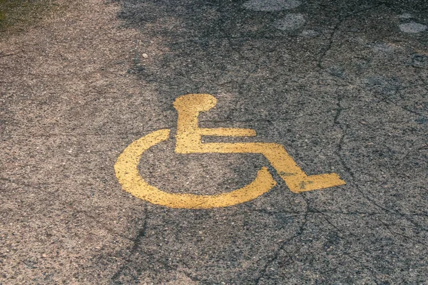 Žlutý symbol invalidního vozíku namalovaného na asfaltu na parkovišti, znamení parkovacího místa pro handicapované návštěvníky. Prázdné vyřazené parkovací místo. — Stock fotografie