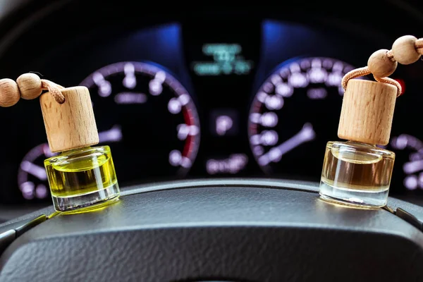 Car air perfume freshener bottles inside the car on the steering wheele. Aromatic liquid in the small bottles. Blurred dashboard lights in the background.