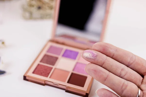 Swatches of eye shadows palette on a female fingers. Blurred white background. Nine colors eye shadow palette.