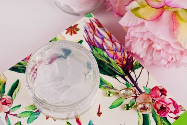 Yumuşak renksiz krem maskeli şeffaf bir kavanoz ya da maske jeli sağda, renkli bir yüzey üzerinde duruyor - büyük pembe bir gül.