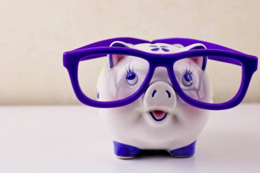 Açık arkaplanda mor gözlük takan kumbara tasarruf, yatırım, bütçe ve finansal konsept olarak kullanılıyor.