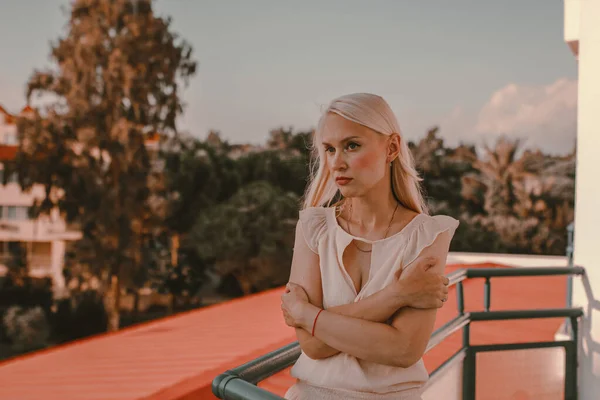 Pensive woman on the balcony. Looking into distance, sad and lonely, waiting for things to be better. Sad blonde woman waiting for someone on the balcony.