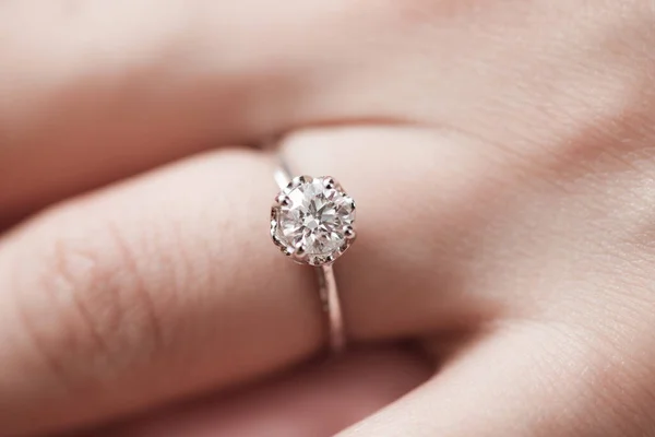 Close up of an elegant engagement diamond ring on woman finger. love, wedding and Valentine\'s day concept. Selective focus with shallow depth of field.