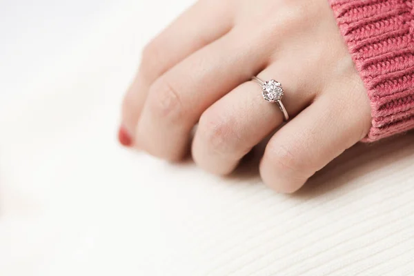Close up of an elegant engagement diamond ring on woman finger with pink sweater winter clothe. love, wedding and Valentine\'s day concept.
