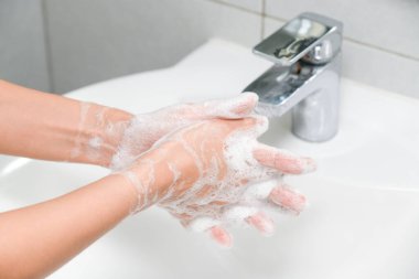 Kadın musluğun altında sabun ve ellerini yıkıyor. Hijyen konsepti el detayı.
