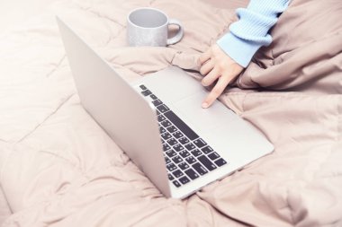 Asyalı kadın el bilgisayarı ve yatağın üzerinde bir fincan kahve kullanıyor. Evde, yatak odasında çalış.