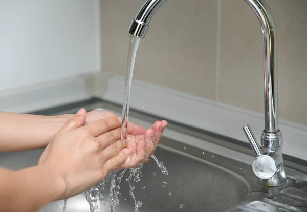 Close up of woman washing her hands in commercial kitchen. Woman washing hands in a sink with tap water