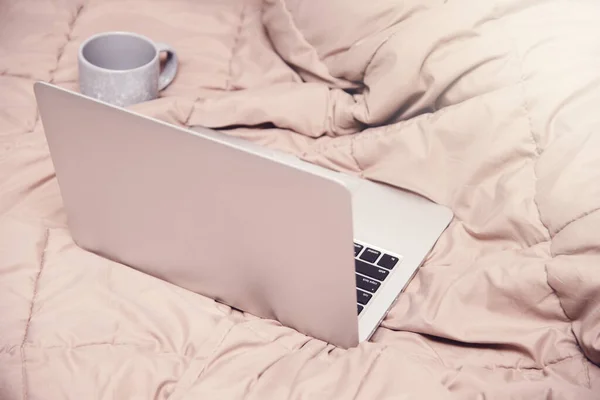 Laptop and a cup of coffee on the bed. Work at home in the bedroom