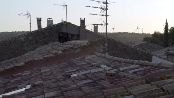 Вид на крышу старого средневекового дома в горной деревне. Каменный дом и черепичная крыша. Ветряные мельницы на заднем плане. Идиотское утро в деревне . — стоковое видео