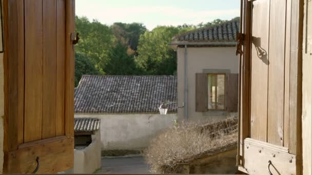 A girl with long hair opens a window overlooking an old village. Idyllic countryside landscape. View of stone houses and tiled roofs. Sunny day. Window with wooden shutters. — Stock Video