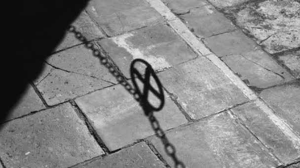 A swinging shadow from a chain fence with a medallion in the shape of a cross. Shadow on the stone pavement. The medieval city. Medieval symbolism. — Stock Video