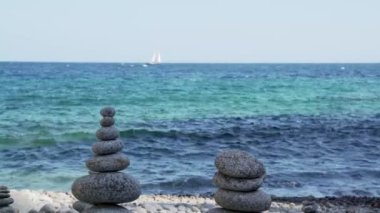 Stone tower on the beach against the azure sea. Beautiful rocks on the background. Peace and tranquility. Clean blue sky. Soul balance. Cobblestone sculptures.