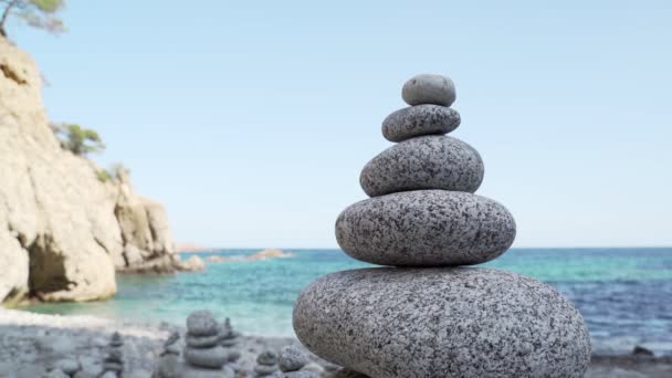 Stone tower on the beach against the azure sea. Beautiful rocks on the background. Peace and tranquility. Clean blue sky. Soul balance. Cobblestone sculptures. — Stok video