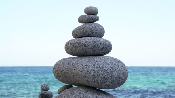 Stone tower on the beach against the azure sea. Beautiful rocks on the background. Peace and tranquility. Clean blue sky. Soul balance. Cobblestone sculptures. — Stok video