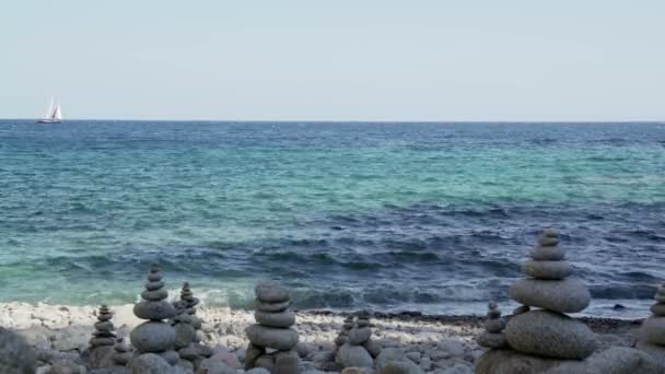 Stone tower on the beach against the azure sea. Beautiful rocks on the background. Peace and tranquility. Clean blue sky. Soul balance. Cobblestone sculptures. — Stok video