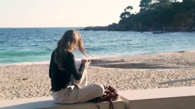 The artist makes sketches on the sunny promenade. Girl draws a coastal landscape with white mediterranean houses. Black and white drawing by liner on white paper. Golden sunlight. Drawing outdoors. 