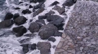 Storm waves hit the rocks at the stone embankment. Dramatic sea. Storm. White sea foam on the stones.