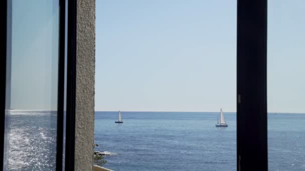 La vista desde la ventana de los yates en el mar. Yates con velas blancas. Deslumbramiento del sol en una ondulación ligera del mar. Clima soleado y mar tranquilo. Hermoso paisaje marino. Tranquilidad y relax . — Vídeos de Stock