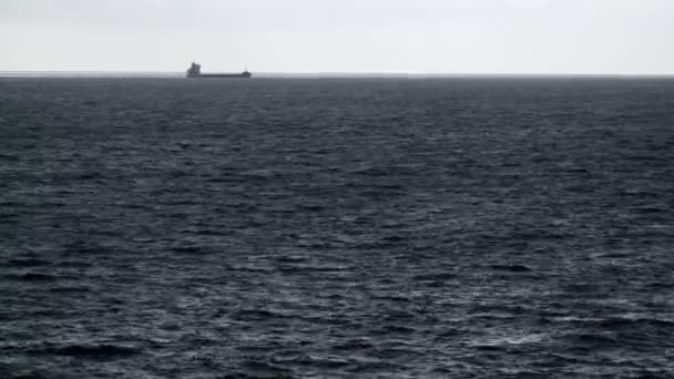 Big ship sailing on the sea on the horizon. Dramatic sea. Strong wind. Clouds run across the sky. Desaturated palette. Sun ripples on the surface of the water. — ストック動画