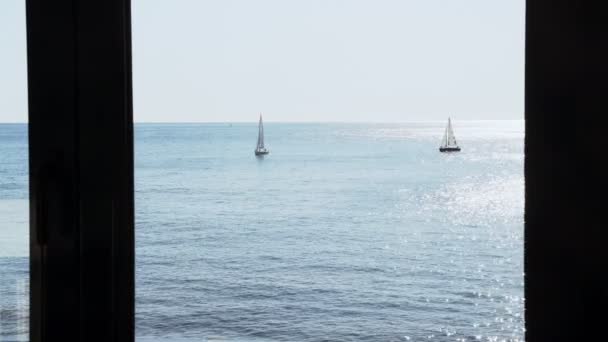 Η θέα από το παράθυρο στα γιοτ στη θάλασσα. Σκάφη με άσπρα πανιά. Ο ήλιος λάμπει σε μια ελαφριά θάλασσα κυματίζει. Ηλιοφάνεια και ήρεμη θάλασσα. Όμορφο θαλάσσιο τοπίο. Ηρεμία και χαλάρωση. — Αρχείο Βίντεο