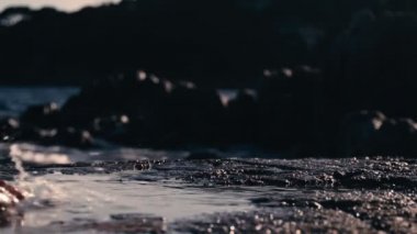 Female bare feet go along the coastal cliffs and step into puddles of water. A splash of water underfoot. Vacations and summer carefree. Walk along the beach. Waves and sea foam in the background.