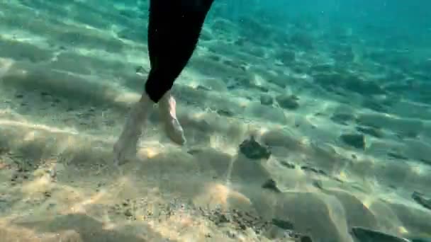 Redhead girl in a black neoprene suit splashes and dance underwater. Sun rays in clear emerald water. Spray and sun glare on the sea sand bottom. Swimming in open water. Beautiful underwater landscape — Stock Video