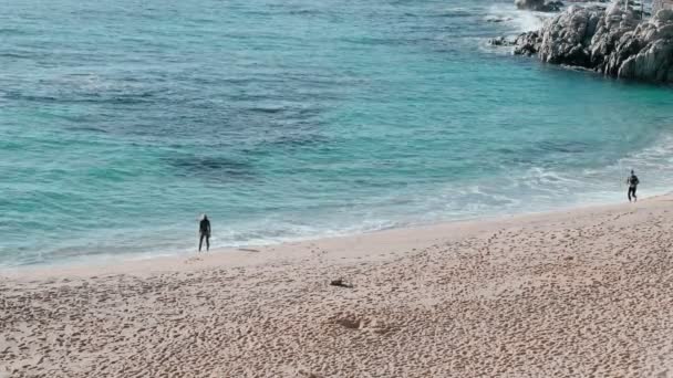 Un couple en néoprène noir s'habille prêt à nager et entre dans l'eau azur. Rayons de soleil dans l'eau claire émeraude dans la belle baie. Spray et éblouissement du soleil. Nager en eau libre. Entraînement de triathlon . — Video