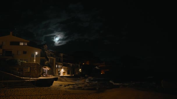 Ночной вид небольшой средиземноморской рыбацкой деревушки. Дурацкое отражение луны в воде. Ночные огни на берегу моря. Волны плескаются в маленькой бухте с небольшой прибрежной деревней. Белые дома — стоковое видео