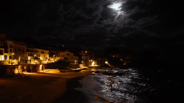 一个小的地中海渔村的夜景。 愚蠢的月亮在水里反射. 海滨的夜灯。 浪花在一个小海湾和一个沿海小村庄里飞溅. 夜海白房子 — 图库视频影像