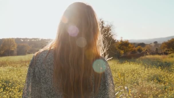 Menina em vestido verde de pé sobre o tolo campo de flores amarelas florescendo. Mulher de cabelo comprido admira a vista da bela paisagem. Luz dourada na paisagem idílica. Paz e tranquilidade . — Vídeo de Stock