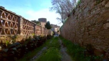 Küçük taştan bir ortaçağ köyünde uzun saçlı bir kız bisikletle yürüyor. Resimli kırsal kesim. Kırsal bisiklet yolculuğu. Eski Stone Caddesi. Altın ışık.