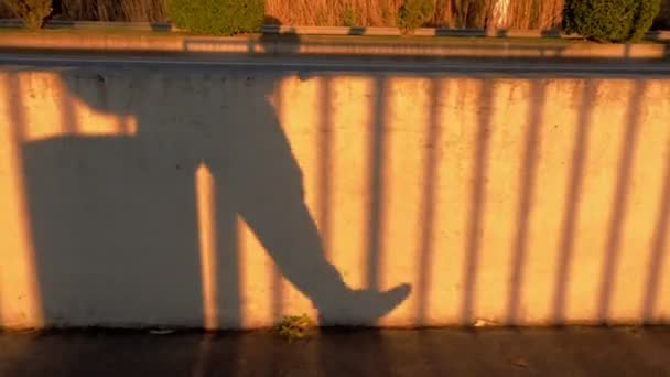 Beton çitin üzerinde yürüyen adam gölgesi. Sarı güneş ışığı ve zıt gölgeler. Yürüyen bacaklar. — Stok video