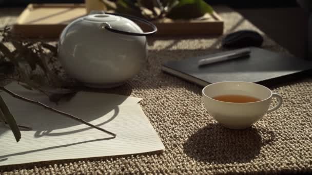 Naturaleza muerta. Una taza de té de hierbas y tetera en la mesa. Té de la mañana. Hermoso desayuno. Rama de eucalipto y cuaderno de bocetos sobre la mesa. Vajilla de porcelana blanca . — Vídeos de Stock