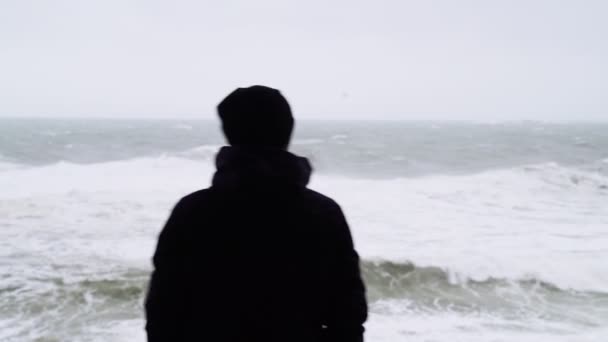 Mannen tittar på det rasande havet. En man bevakar stormen. Silhuett av en man. Svårt stormigt hav. Stora vågor. Vindstarkt regnigt väder. Utsikt över det dramatiska havet. Vinden blåser. — Stockvideo