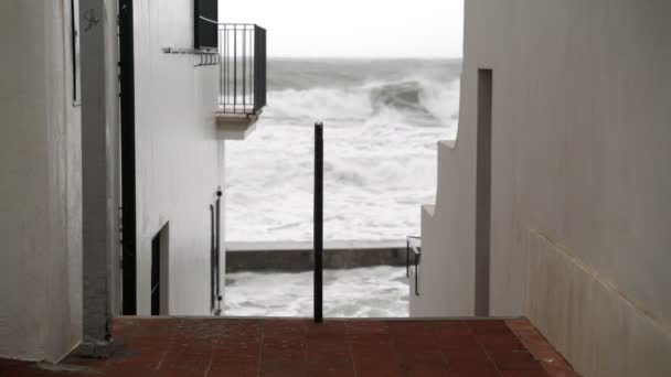 Άποψη της φουρτουνιασμένης θάλασσας από τα στενά δρομάκια μιας μικρής πόλης. Βλέποντας την καταιγίδα. Μικρό χωριό κατά τη διάρκεια μιας καταιγίδας. Έντονη θάλασσα. Μεγάλα κύματα. Άνεμος βροχερός καιρός. Άποψη του δραματικού ωκεανού. — Αρχείο Βίντεο