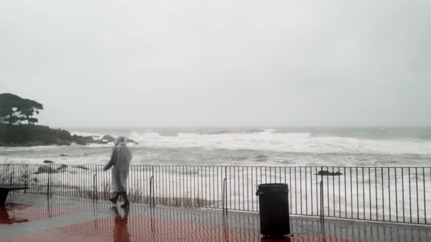 Dziewczyna w białym płaszczu idzie burzliwym morzem. Kobieta obserwuje burzę. Młoda kobieta spacerująca nad morzem. Silne burzliwe morze. Duże fale. Silny wiatr. Wiatr deszczowa pogoda. — Wideo stockowe