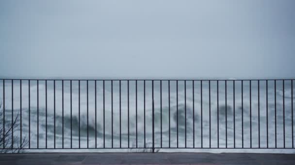 遊歩道からの荒波の眺め。波が海岸を襲った。嵐を見てる嵐の中の小さな村激しい荒れ狂う海大きな波だ風の強い雨の天気。劇的な海の眺め. — ストック動画